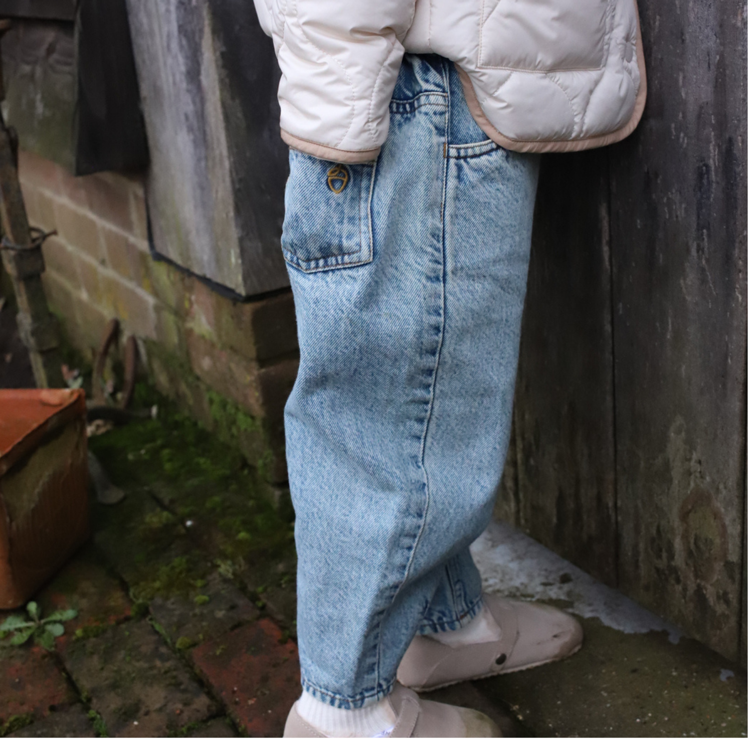 Girl wearing NELBEE light blue jeans and a white puffer jacket in an outdoor setting.